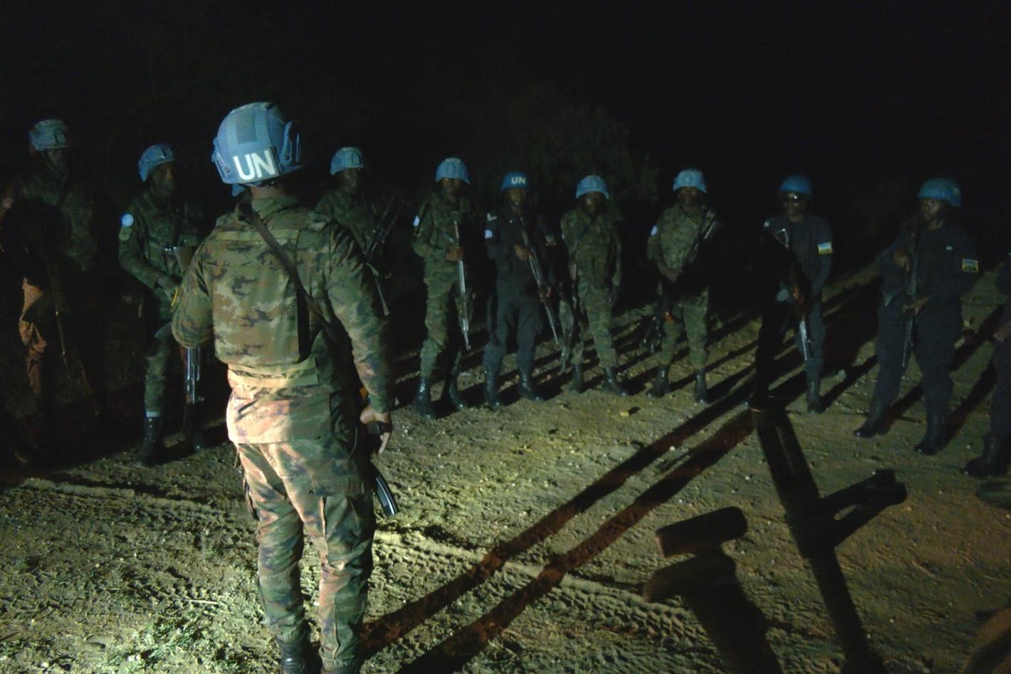 A group of peacekeepers standing together in a group with one peacekeeper leading the discussion. It is nighttime in the photo.