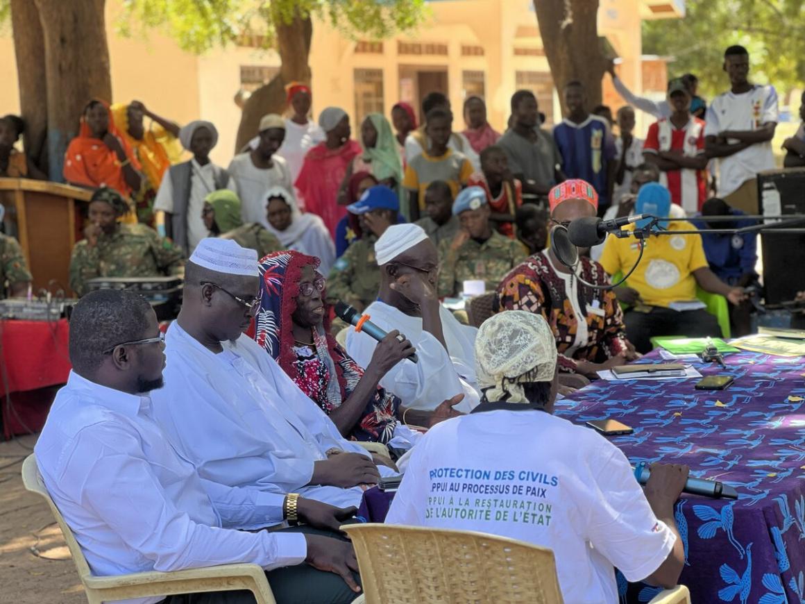 A group of people sit around a table, speaking into microphones in front of cummunity members