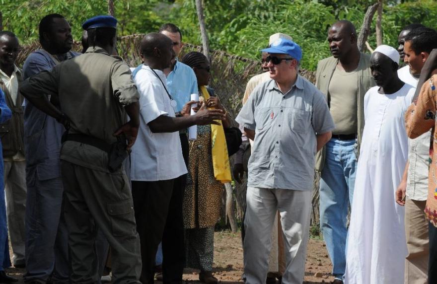 UN staff gather near a white tent with sandbags and a thatched roof.